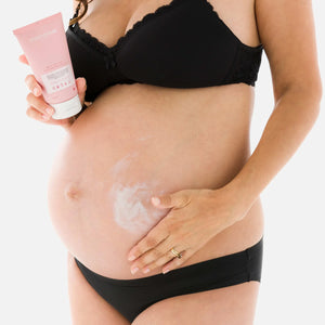 Pregnant woman holding Mamalove Belly Butter in one hand while applying it to her pregnant belly with the other, demonstrating how the cream spreads smoothly without leaving any stains.