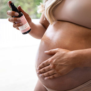 Pregnant woman holding Mamalove Body Oil in her hand, showcasing her glossy baby bump with hydrated, glowing skin.